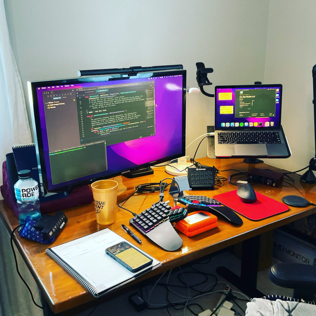 Mikaela's desk with a monitor, laptop setting on a stand, and split keyboard